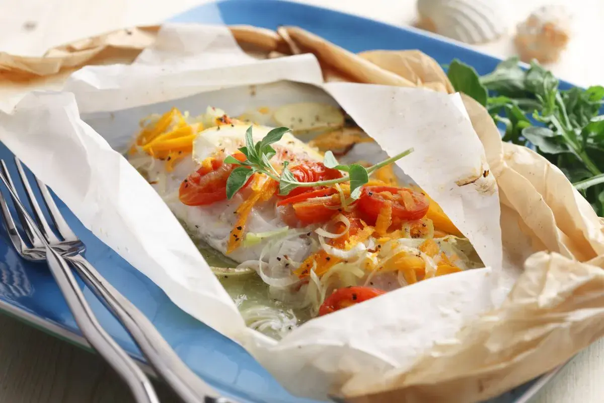 Un plat de cabillaud en papillote, garni de tomates cerises et d'herbes. Un délice pour savoir quel vin avec du cabillaud.