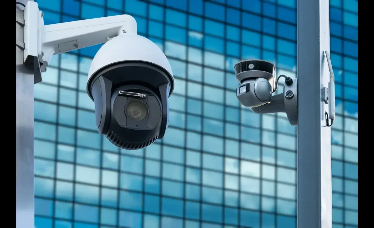 Deux caméras de vidéosurveillance entreprise montées sur un poteau, avec un bâtiment moderne en arrière-plan.
