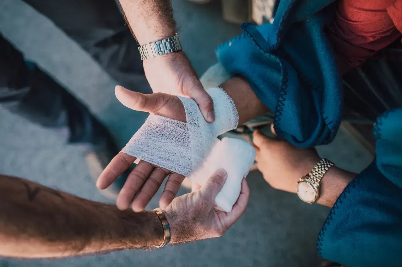 Mains bandant une blessure, peut-être suite à une violence involontaire. L'une des mains est bandée, l'autre tient la compresse.