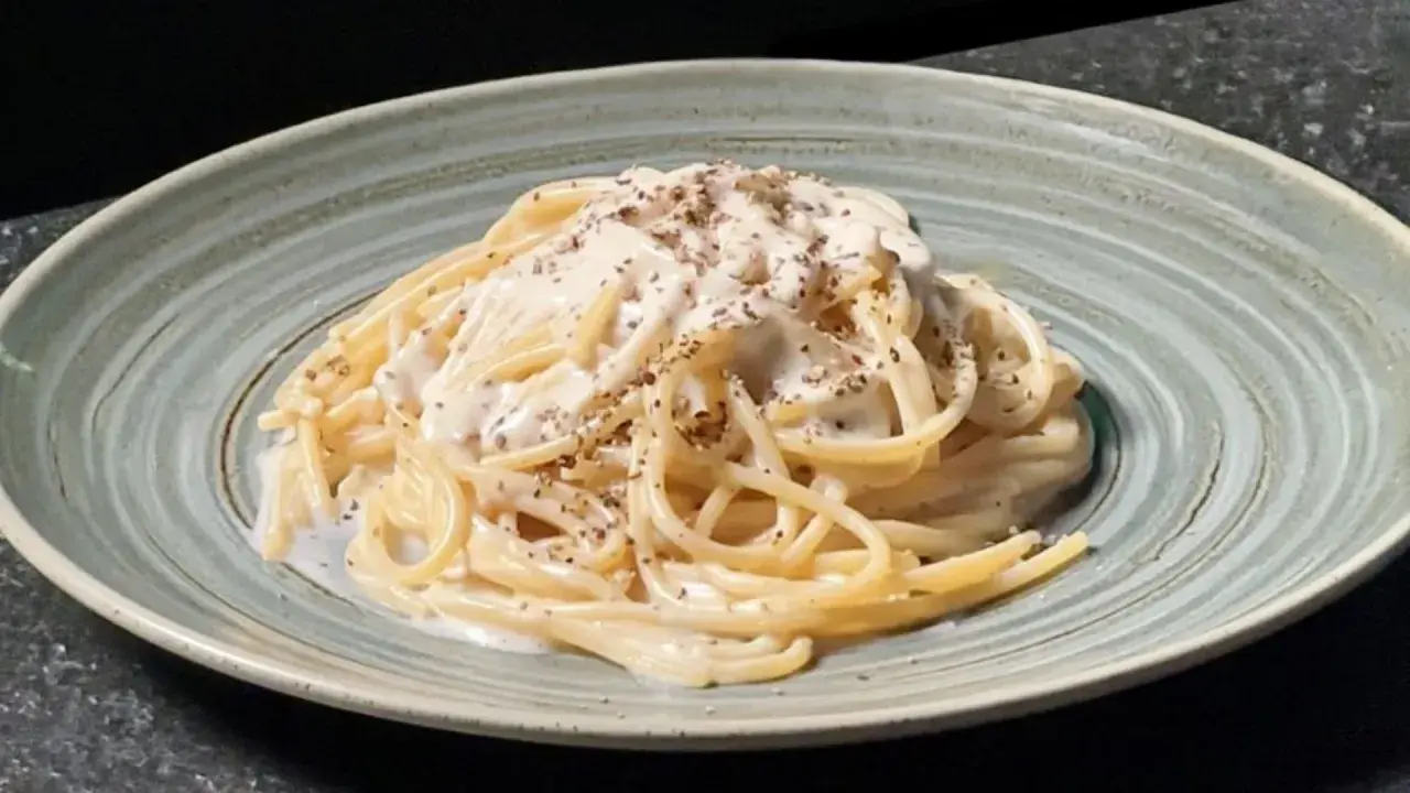 Un plat de tonnarelli cacio e pepe crémeux, saupoudré de poivre noir fraîchement moulu, servi dans une assiette texturée.