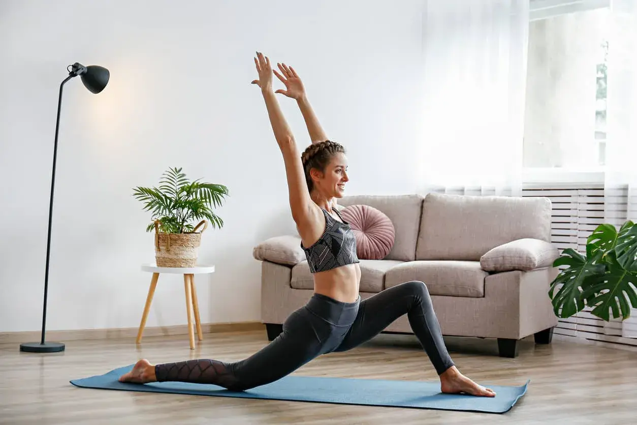 Une femme souriante pratique le yoga à la maison, profitant des bienfaits de cette discipline pour son bien-être.