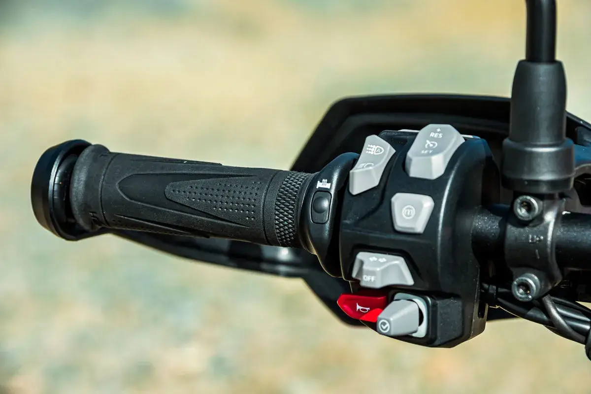 Mandos de la moto: puño negro texturizado y panel de control con botones grises y rojos para luces, crucero y bocina.