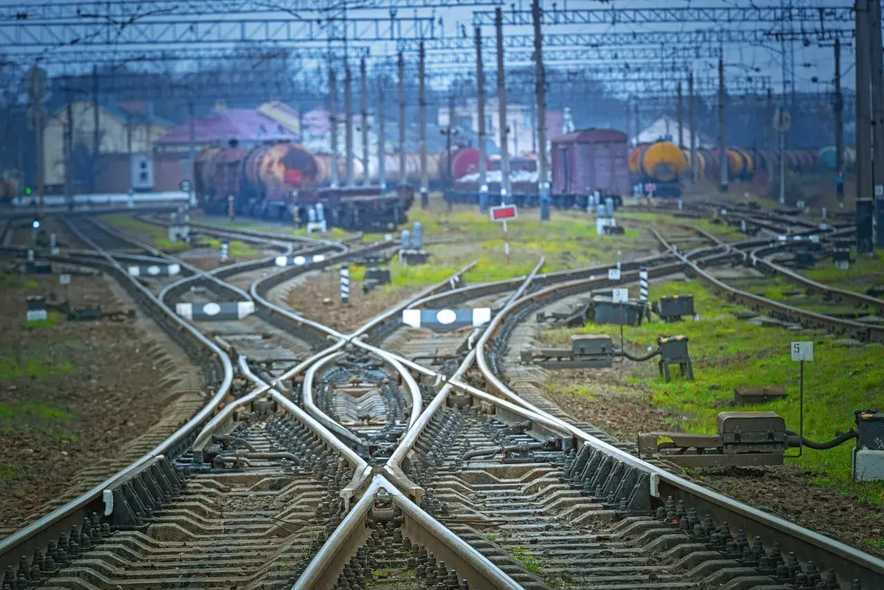 Skrzyżowanie torów kolejowych z widocznym wskaźnikiem W20. W tle stoją wagony towarowe.