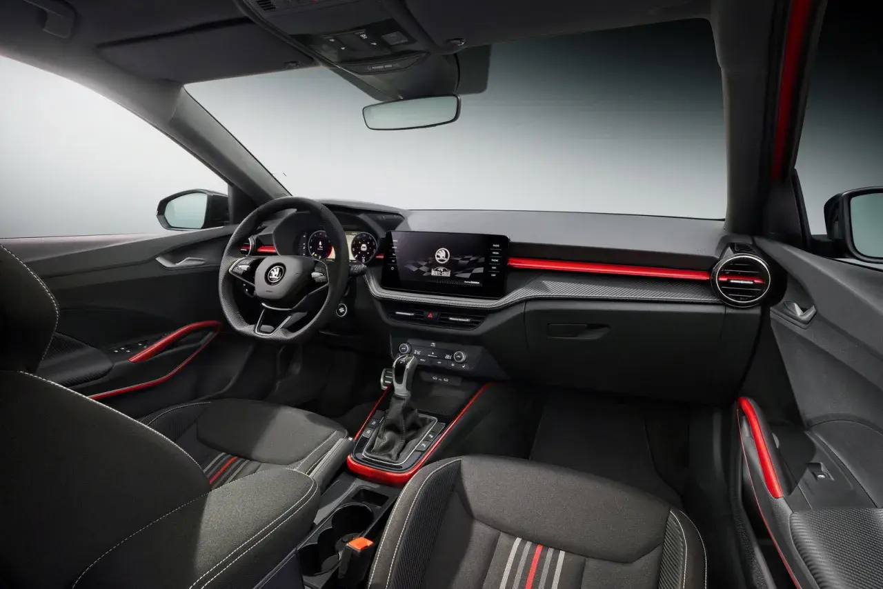 Interni sportivi della Skoda Fabia Montecarlo con sedili in tessuto, volante multifunzione e display centrale. Dettagli rossi accentuano l'abitacolo.