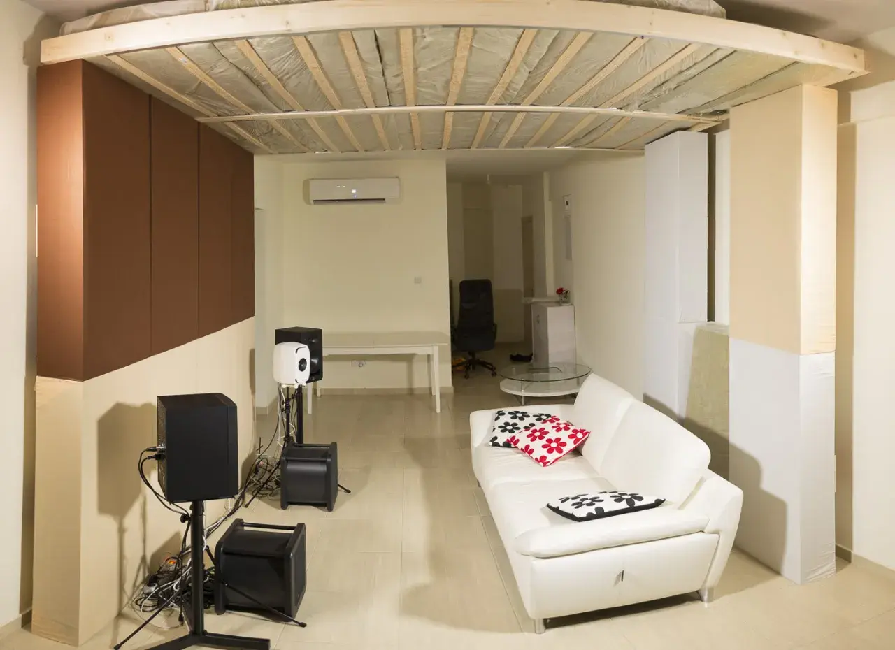 Ein Raum mit weißem Ledersofa, Lautsprechern und einer Deckenkonstruktion, die an ein **Deckensegel selber bauen** Projekt erinnert.