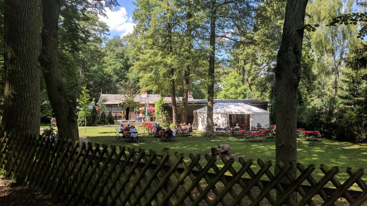 Ein Biergarten im Grünen, mit Gästen an Tischen unter Bäumen und einem Festzelt. Hier findet man **hanffs ruh**.