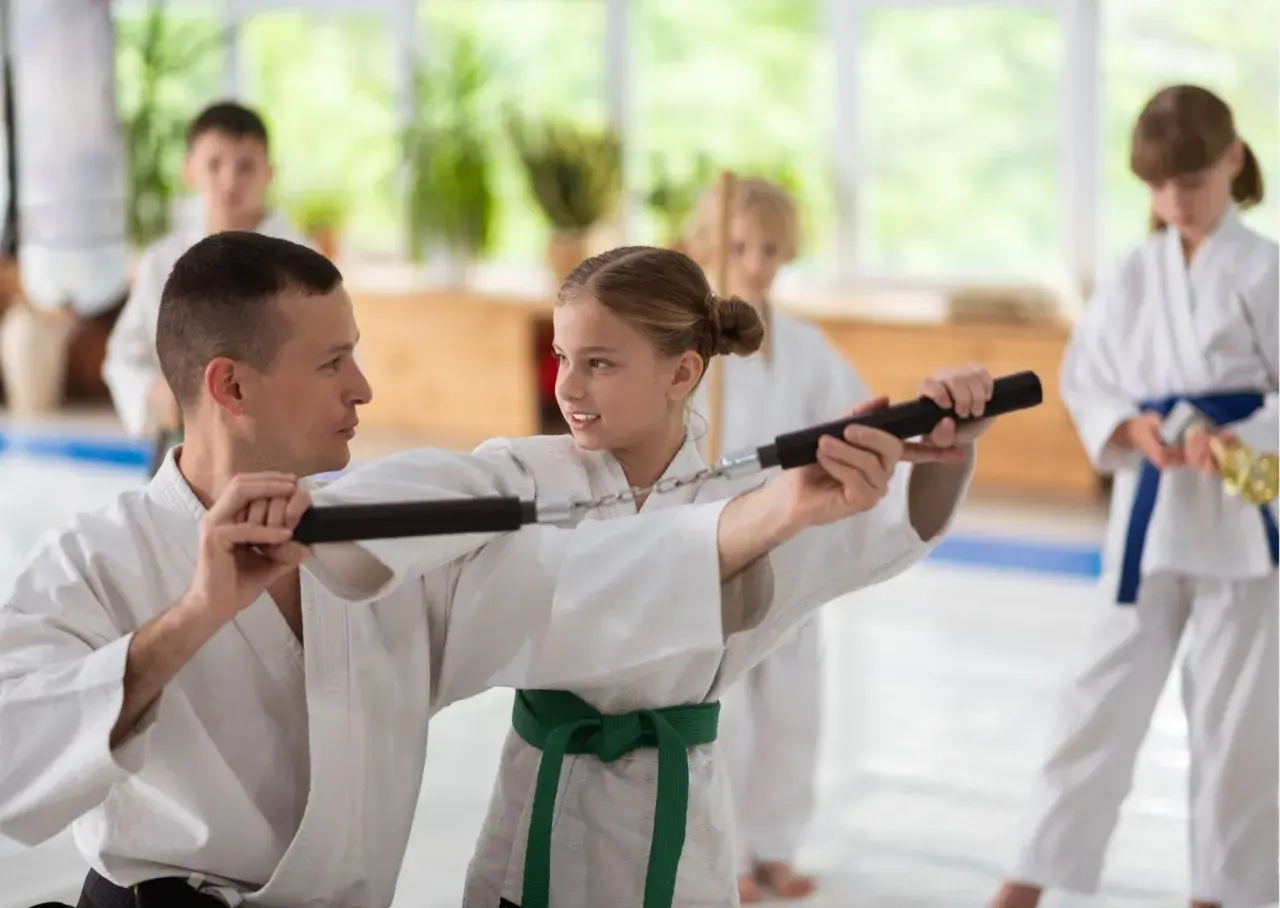 Nauczyciel pokazuje dziewczynce, jak używać nunchaku podczas treningu sztuk walki.