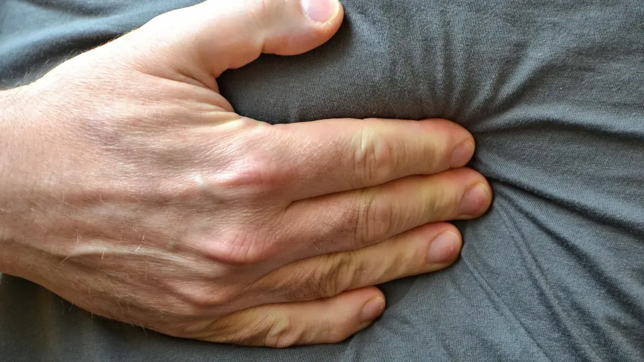 Eine Hand drückt auf den Bauch, was auf Beschwerden wie bei einer Lebensmittelunverträglichkeit hindeuten könnte.