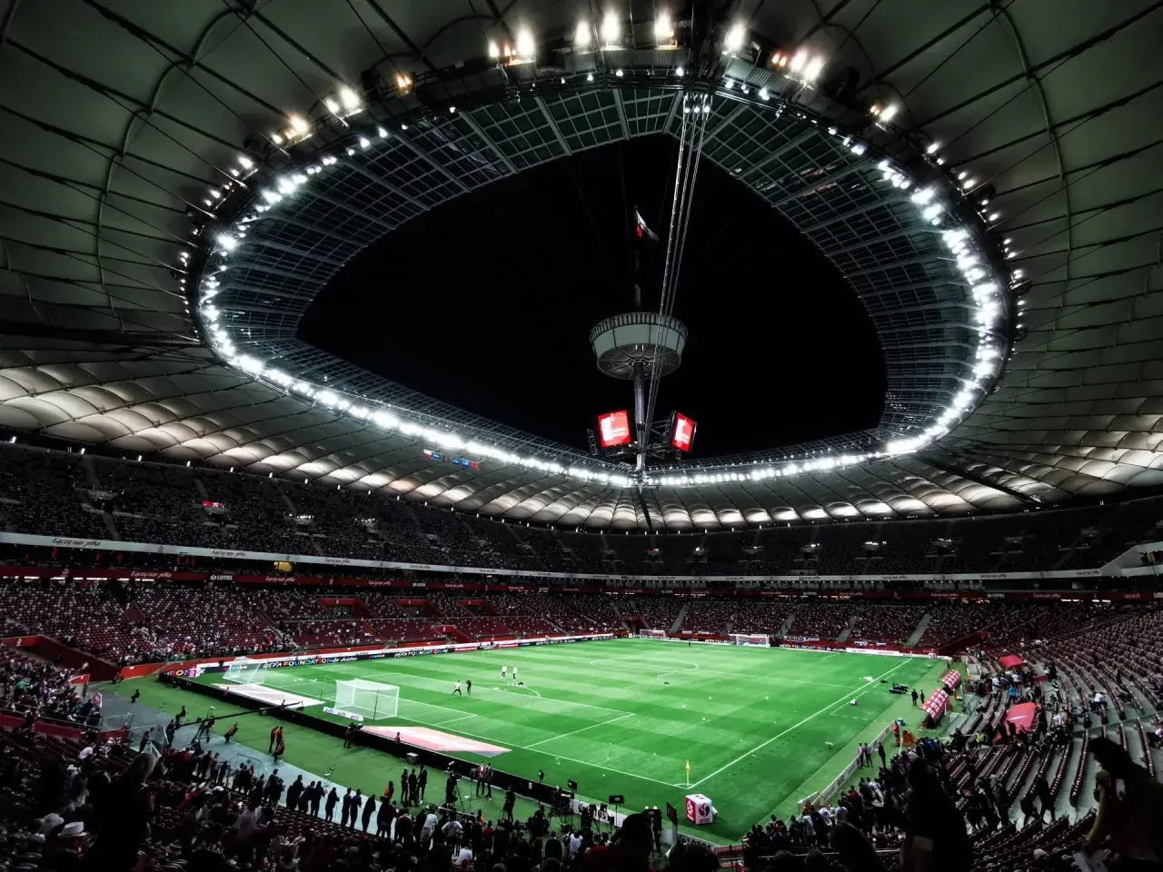 Widok na murawę i trybuny największego stadionu w Polsce. Rozświetlony dach i jupitery tworzą niesamowitą atmosferę.