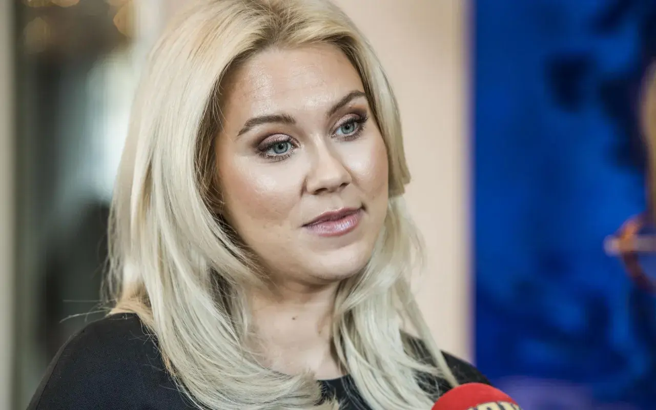 Caroline Hainer, med blont hår och makeup, ser åt sidan. En mikrofon syns i förgrunden.