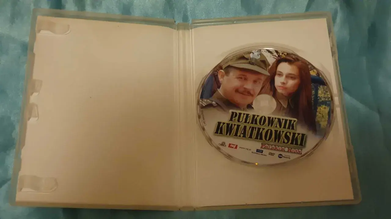 Płyta DVD z filmem "Pułkownik Kwiatkowski" i jego obsadą. Widoczni są główni bohaterowie, pułkownik i młoda kobieta.
