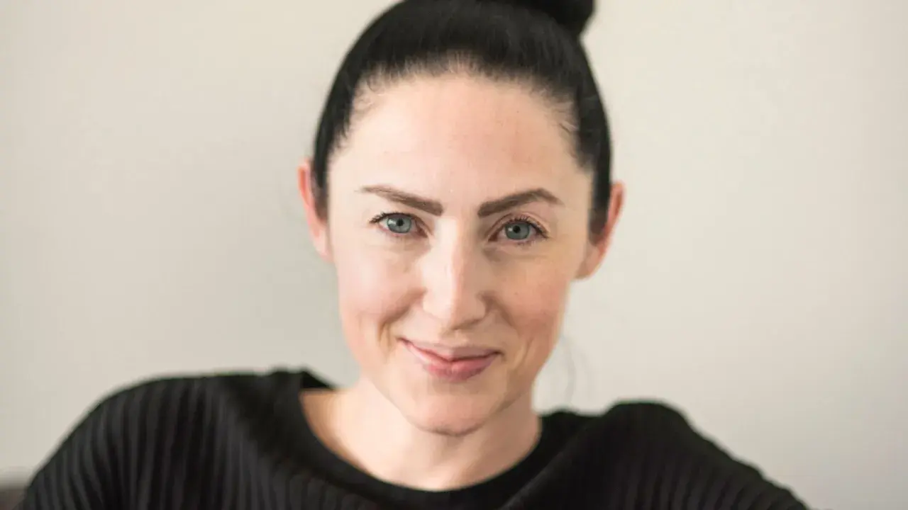 Emma Gray Munthe, med håret uppsatt i en knut, ler mot kameran. Hon bär en svart, ribbad tröja.