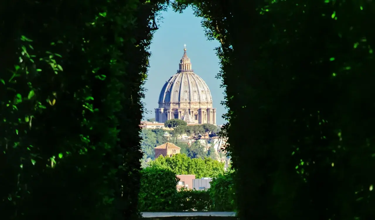 Blick durch grüne Hecken auf die Kuppel des Petersdoms. Ein versteckter Aussichtspunkt, einer der vielen Rom Geheimtipps.