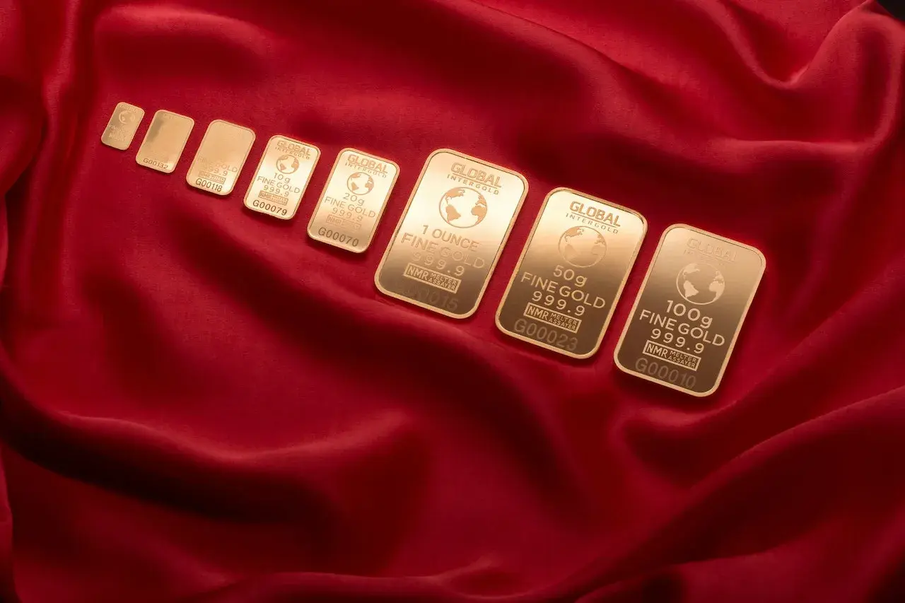 Sztabki złota Global Intergold, od najmniejszej do 100g, ułożone na czerwonym jedwabiu. Wśród nich widać combibar Valcambi.