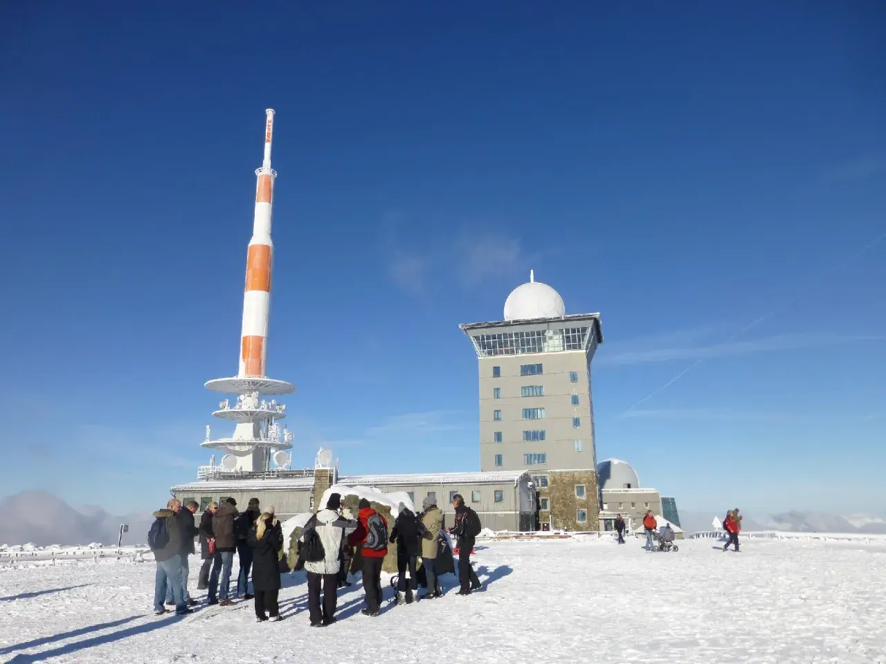 Menschen stehen im Schnee vor dem Brocken-Wetterturm und dem Fernsehturm. Ein sonniger Tag im Winter auf dem Brocken.