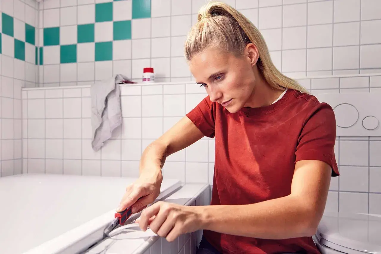 Frau entfernt mit einem Cuttermesser alte Silikonfugen an der Badewanne.