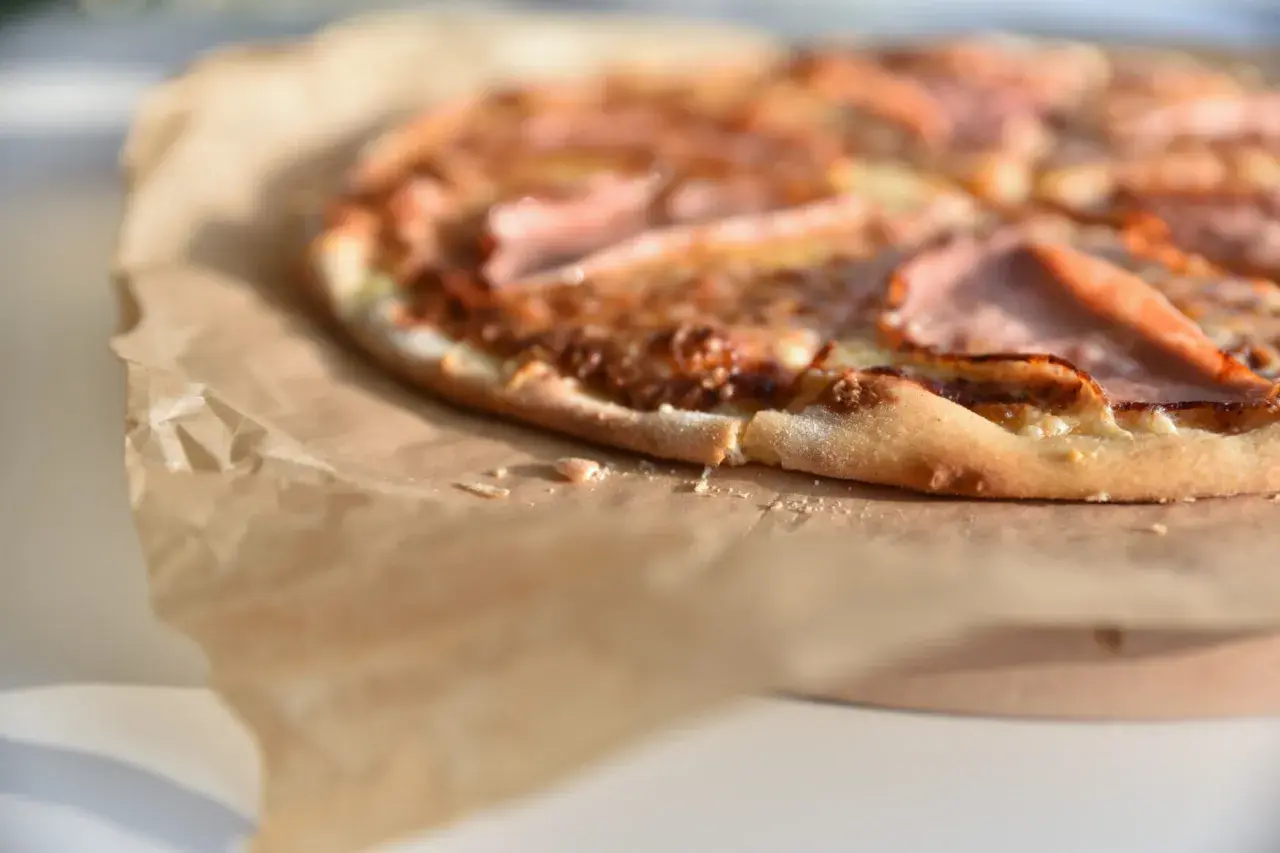 Zbliżenie na pizzę z szynką na papierze do pieczenia.