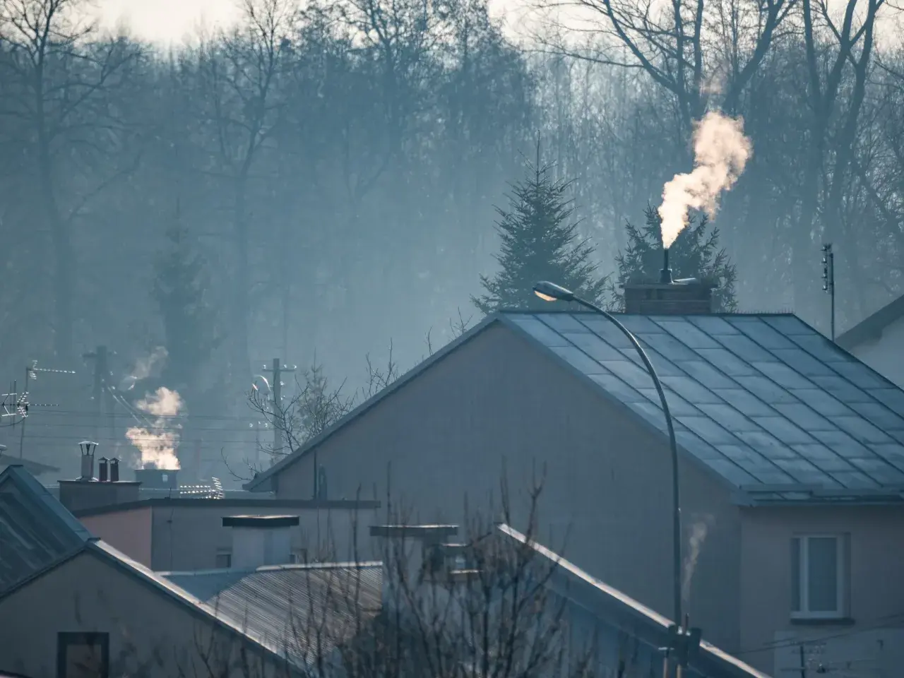 Dym z komina nad domami, czy spaliny z pieca gazowego są szkodliwe? Mglisty poranek nad miastem.