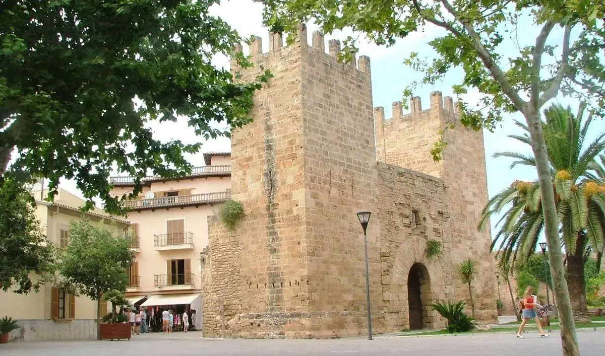 Kamienne mury Alcudia stare miasto, z palmami i budynkami w tle.