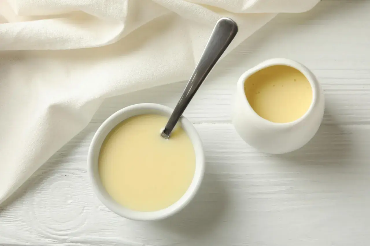 Crema amarilla en un cuenco con cuchara y jarrita, ideal para sustituir nata para cocinar por leche en recetas ligeras.
