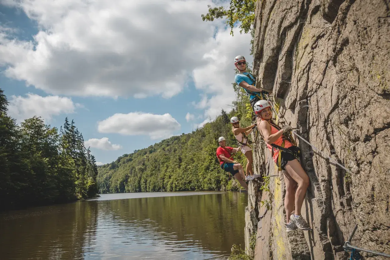 Grupa przyjaciół pokonuje via ferrata w Czechach, wspinając się po skalnej ścianie nad malowniczą rzeką.