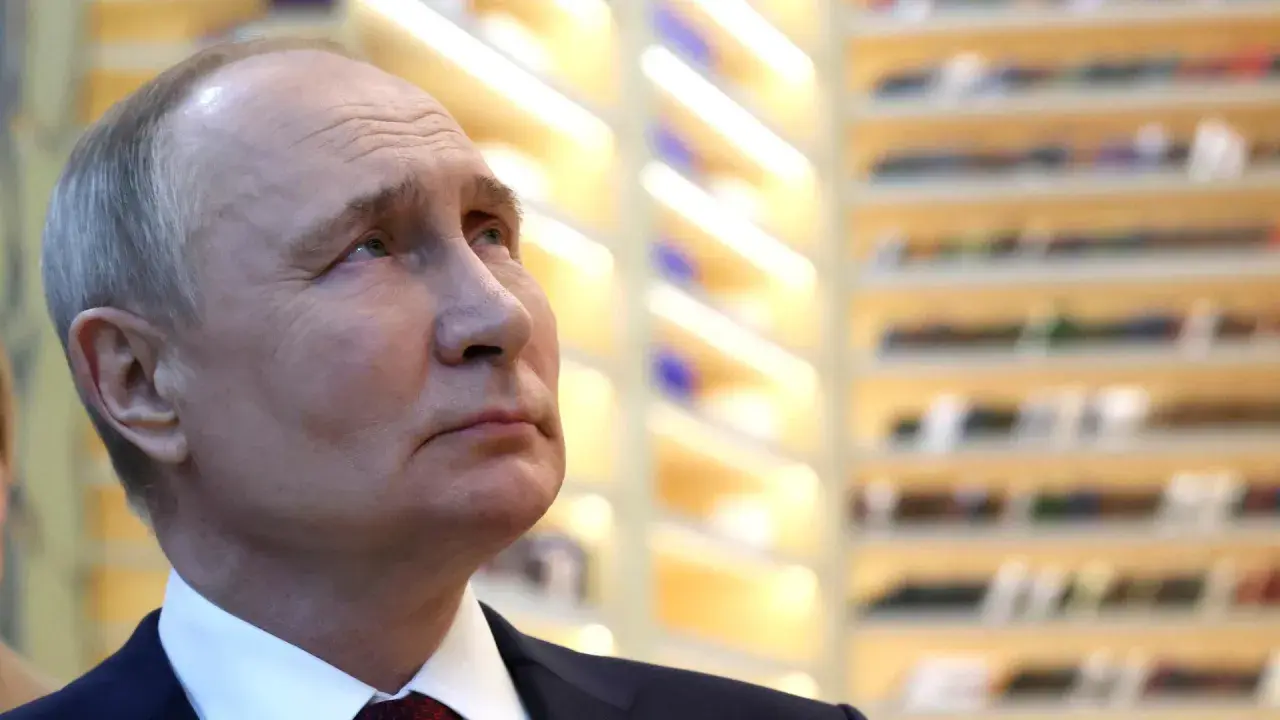 Nahaufnahme von Wladimir Putin, der nachdenklich in die Ferne blickt. Die Hintergrundbeleuchtung deutet auf eine Veranstaltung hin, vielleicht im Zusammenhang mit den Russland Wahlen.