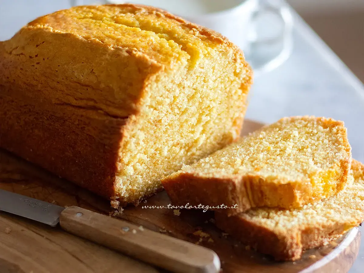 Plumcake senza yogurt dorato e soffice, tagliato a fette su un tagliere di legno con un coltello.