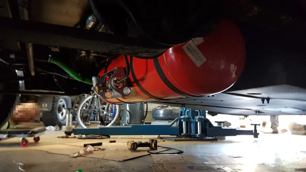 Installation d'un réservoir GPL sous un camping-car, respectant la réglementation GPL camping-car. Le réservoir rouge est visible, fixé sous le châssis.