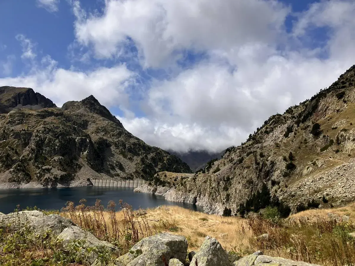 Paisaje montañoso con un embalse azul, ideal para rutas en Sallent de Gállego. Nubes y vegetación agreste completan la escena.