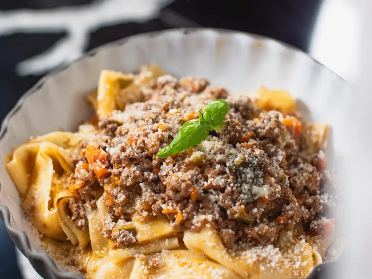 Un plat de pâtes fraîches, garni d'une sauce bolognaise riche et savoureuse, parsemé de parmesan et d'une feuille de basilic. Une recette spaghetti bolognaise italienne authentique.