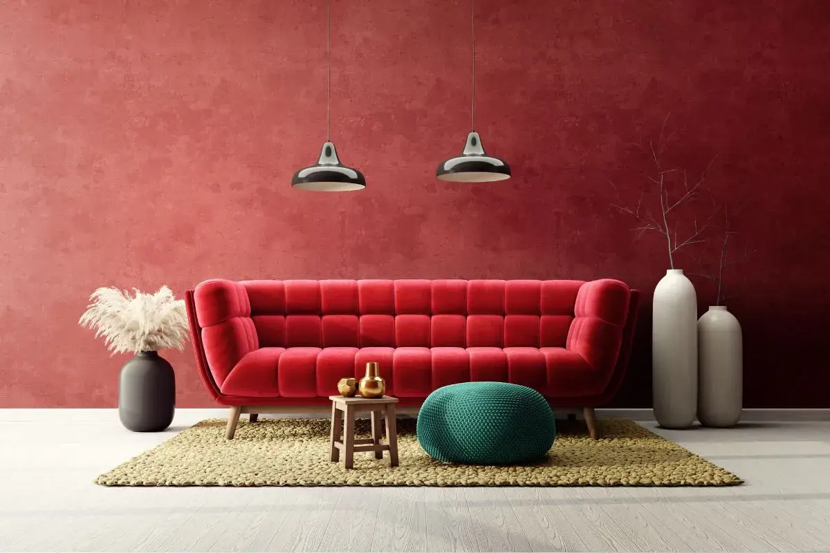 Soggiorno moderno con divano rosso vellutato e **effetto spugnato muro** color bordeaux. Due lampade a sospensione, pouf verde acqua e vasi bianchi completano l'arredo.