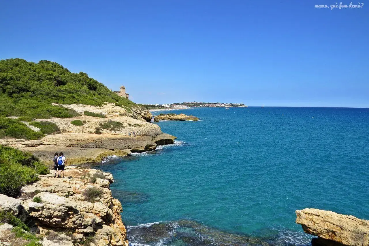 Dos personas caminan por el camí de ronda en Tarragona, disfrutando de las vistas al mar Mediterráneo y la costa.