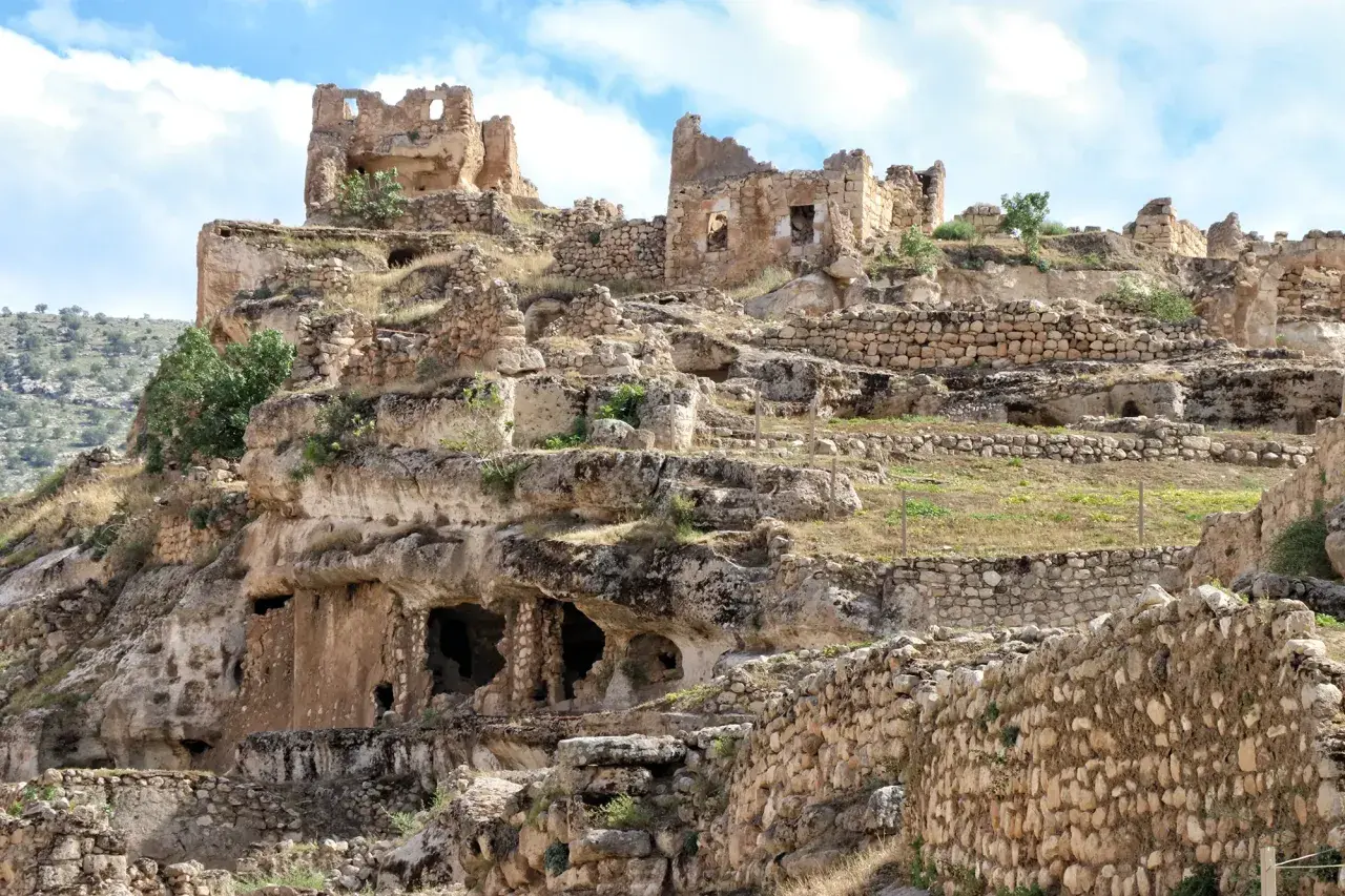 Ruiny starożytnego miasta Hasankeyf na skalistym zboczu, z widocznymi jaskiniami i kamiennymi murami.