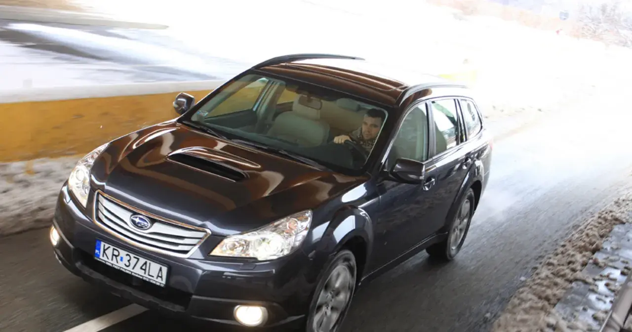Ciemny Subaru Outback 2025 jedzie przez tunel, kierowca w szaliku.