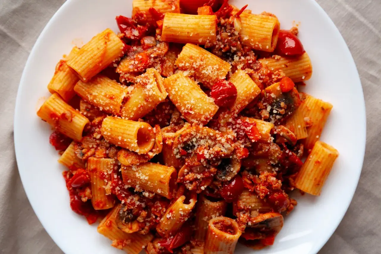 Pyszny obiad z mięsa mielonego z makaronem rigatoni w sosie pomidorowym, posypany parmezanem.