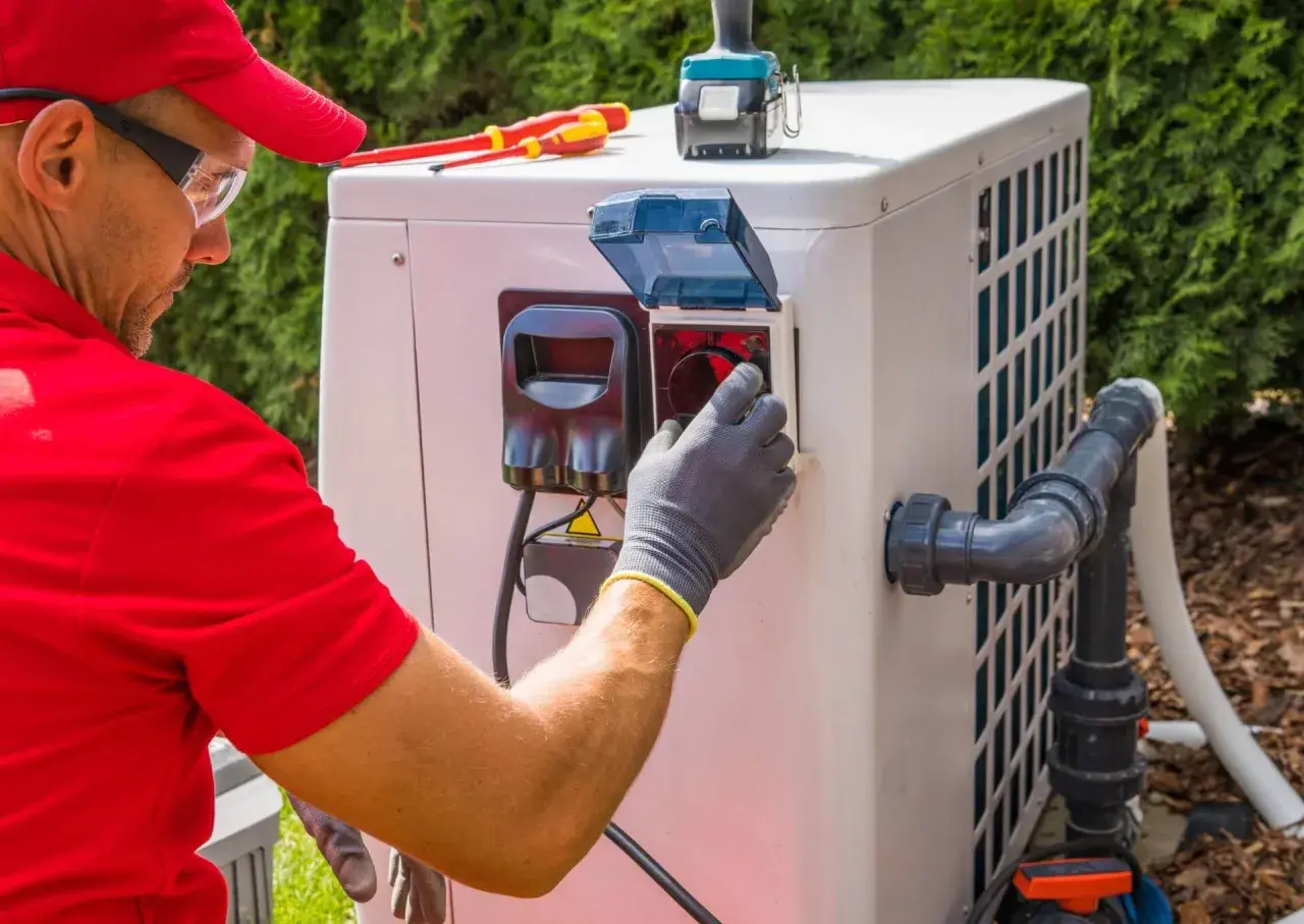 Technik w rękawiczkach sprawdza panel pompy ciepła, by zapewnić optymalną, jaką temperaturę daje pompa ciepła. Narzędzia leżą obok.
