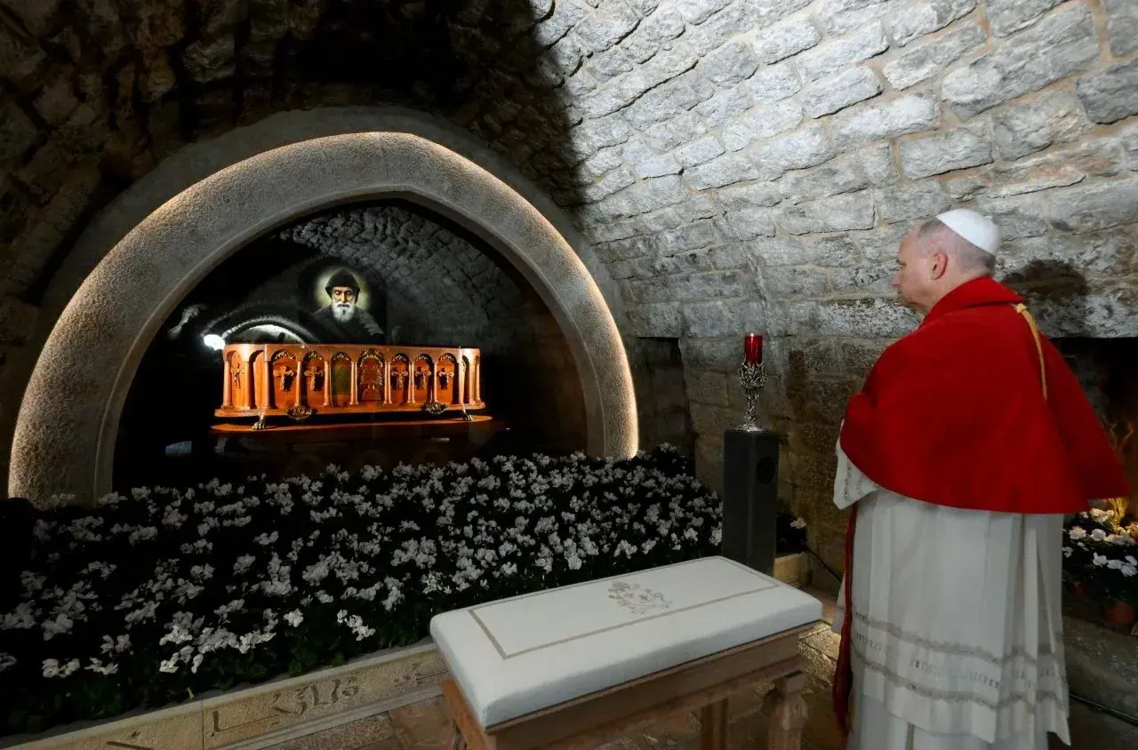 28 lipca. Papież w czerwonym płaszczu stoi przed grobowcem z portretem świętego i białymi kwiatami.