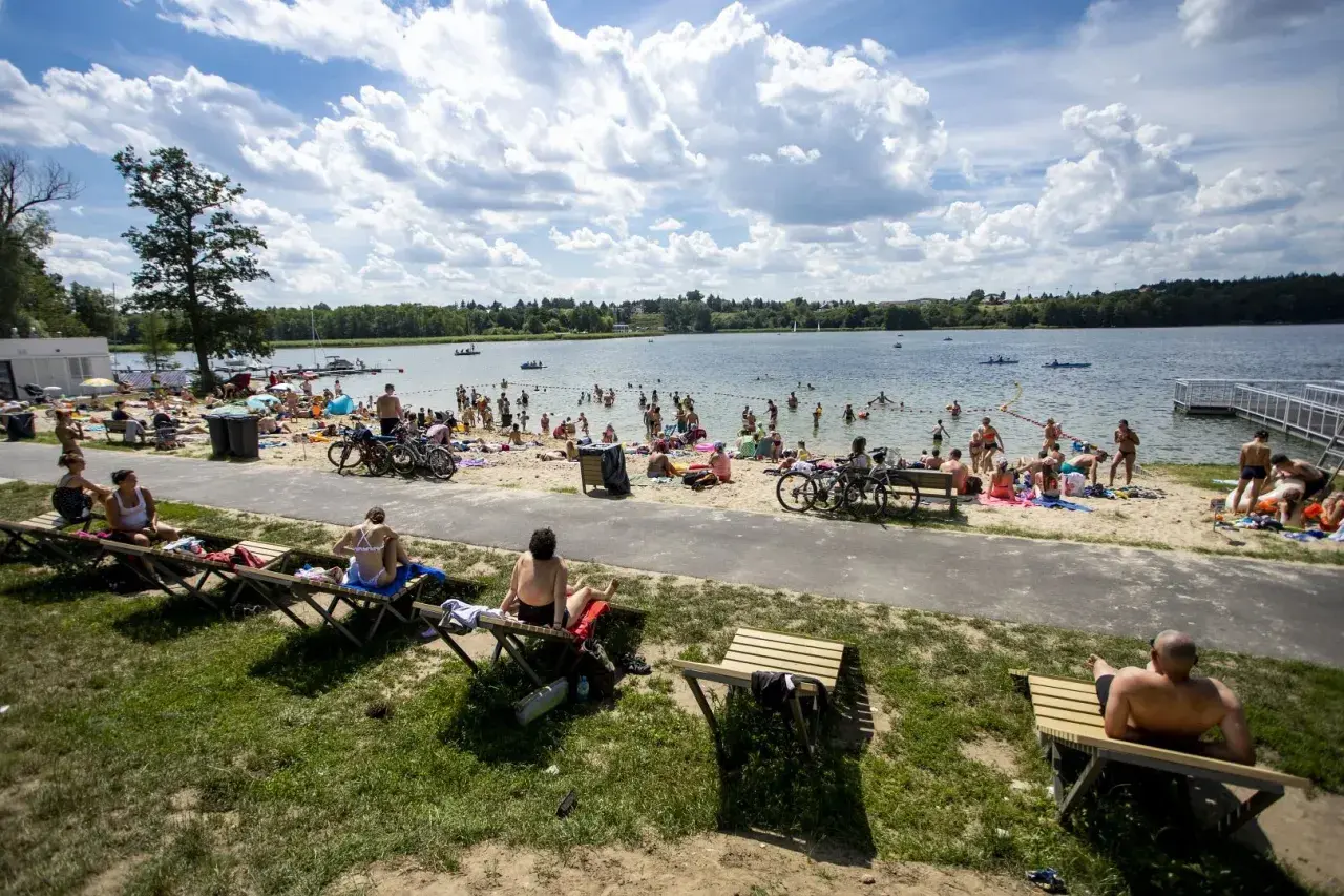 Tłum ludzi odpoczywa na plaży nad jeziorem Kierskim Małym. Słońce świeci, a chmury tworzą malowniczy krajobraz.
