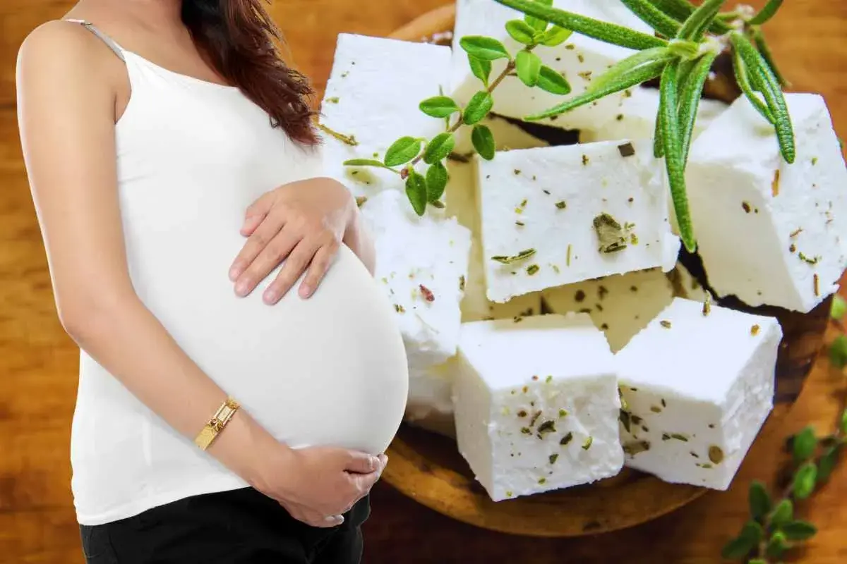 Pancia di donna incinta accarezzata, con cubetti di feta aromatizzata alle erbe sullo sfondo.