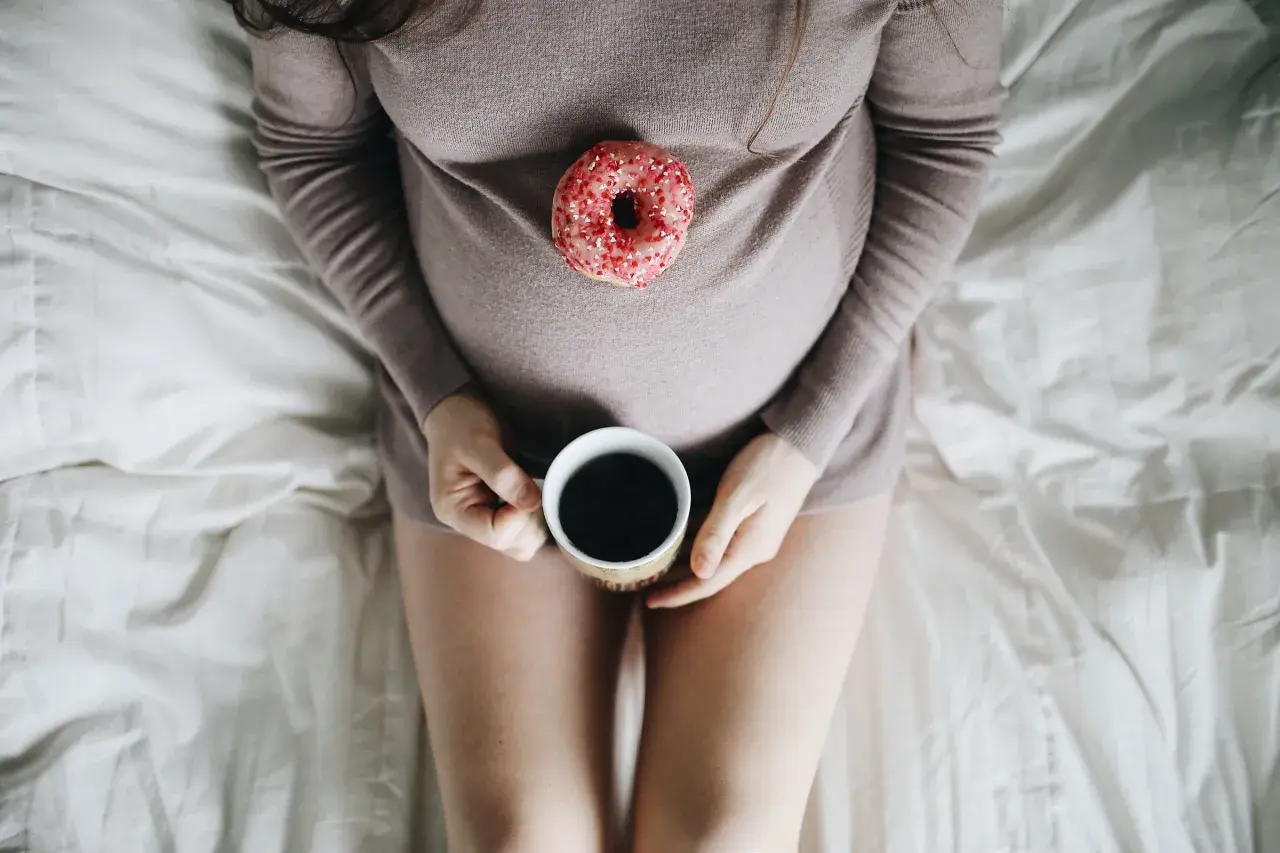 En gravid mage med en donut och en kopp kaffe. En stunds avkoppling innan amning.