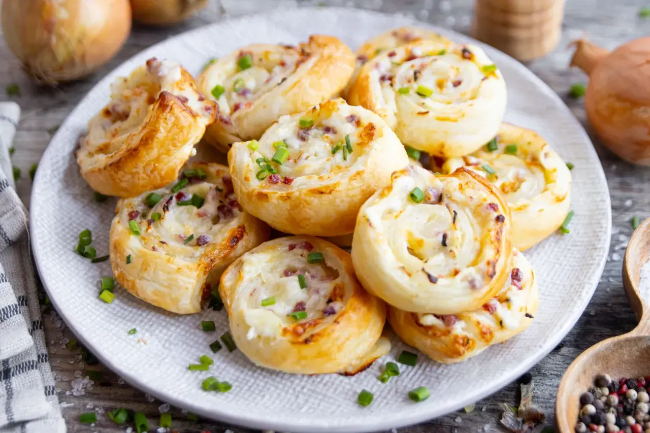 Herzhafte Flammkuchen Schnecken mit Speck und Zwiebeln, bestreut mit frischem Schnittlauch, auf einem Teller angerichtet.