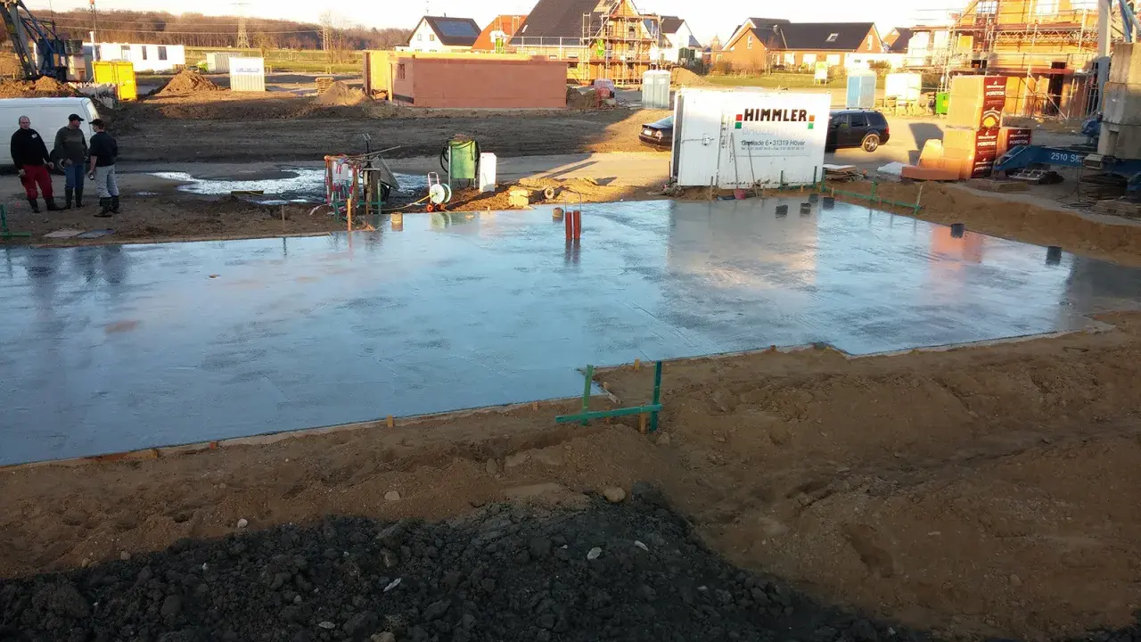 Frisch gegossene Betonplatte auf einer Baustelle. Verschiedene Arten von Bewehrung sind sichtbar, die für Stabilität sorgen.