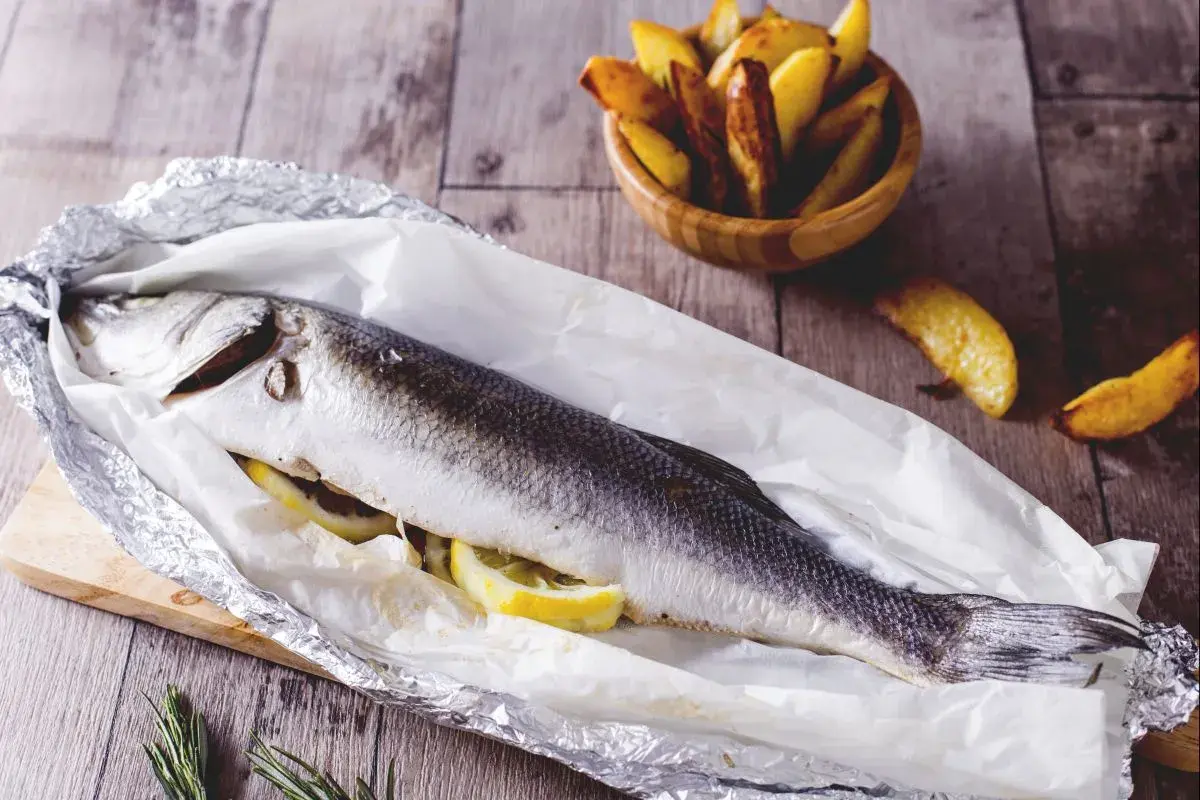 Gegrillter Seebarsch mit Zitrone, bereit für den köstlichen Geschmack. Dazu knusprige Kartoffelspalten.