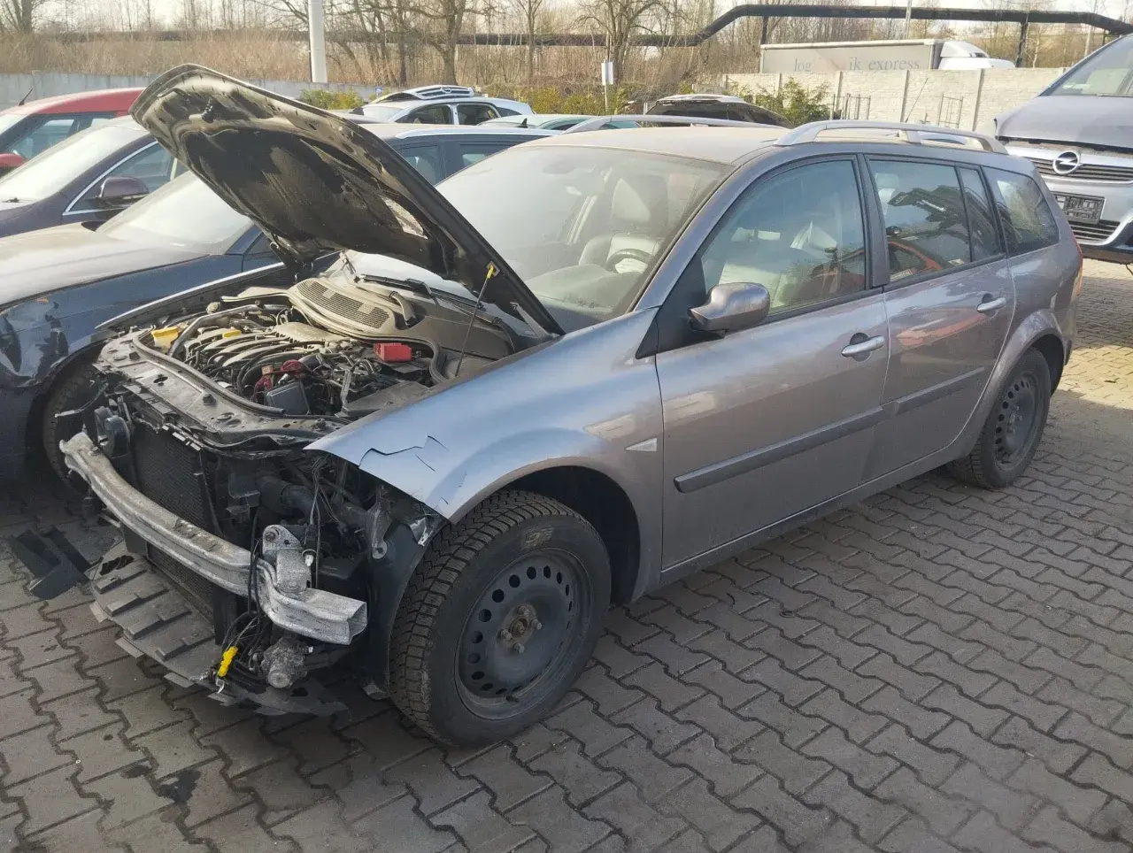 Szary kombi z otwartą maską, widoczny silnik i uszkodzony przód. Idealny, by dowiedzieć się, jak sprzedać auto na części.