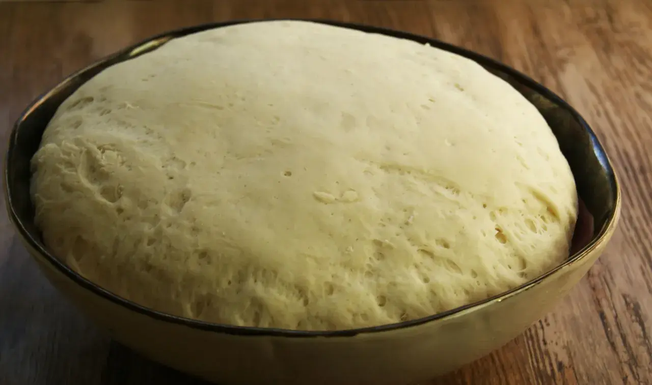 Puszyste ciasto na pizzę wyrosło w misce, gotowe do dalszej obróbki.
