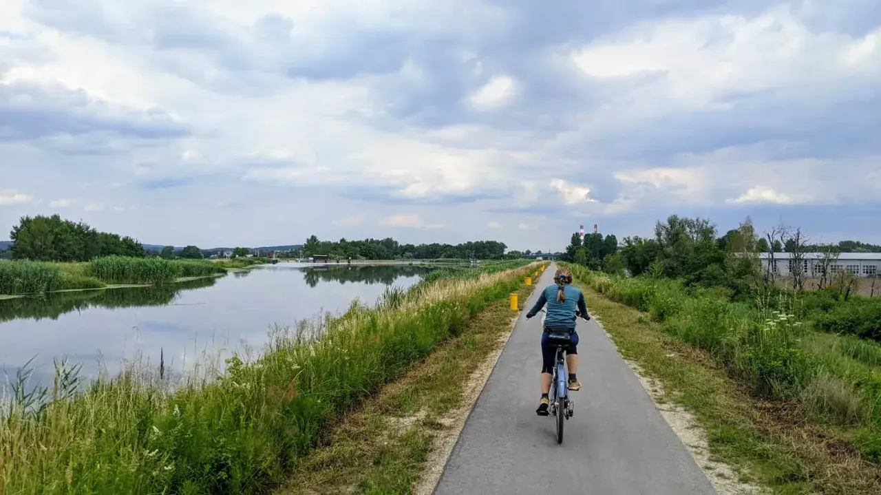 Kobieta na rowerze przemierza ścieżkę nad wodą, ciesząc się pięknem przyrody. To idealne miejsce na **velo Skawina**.