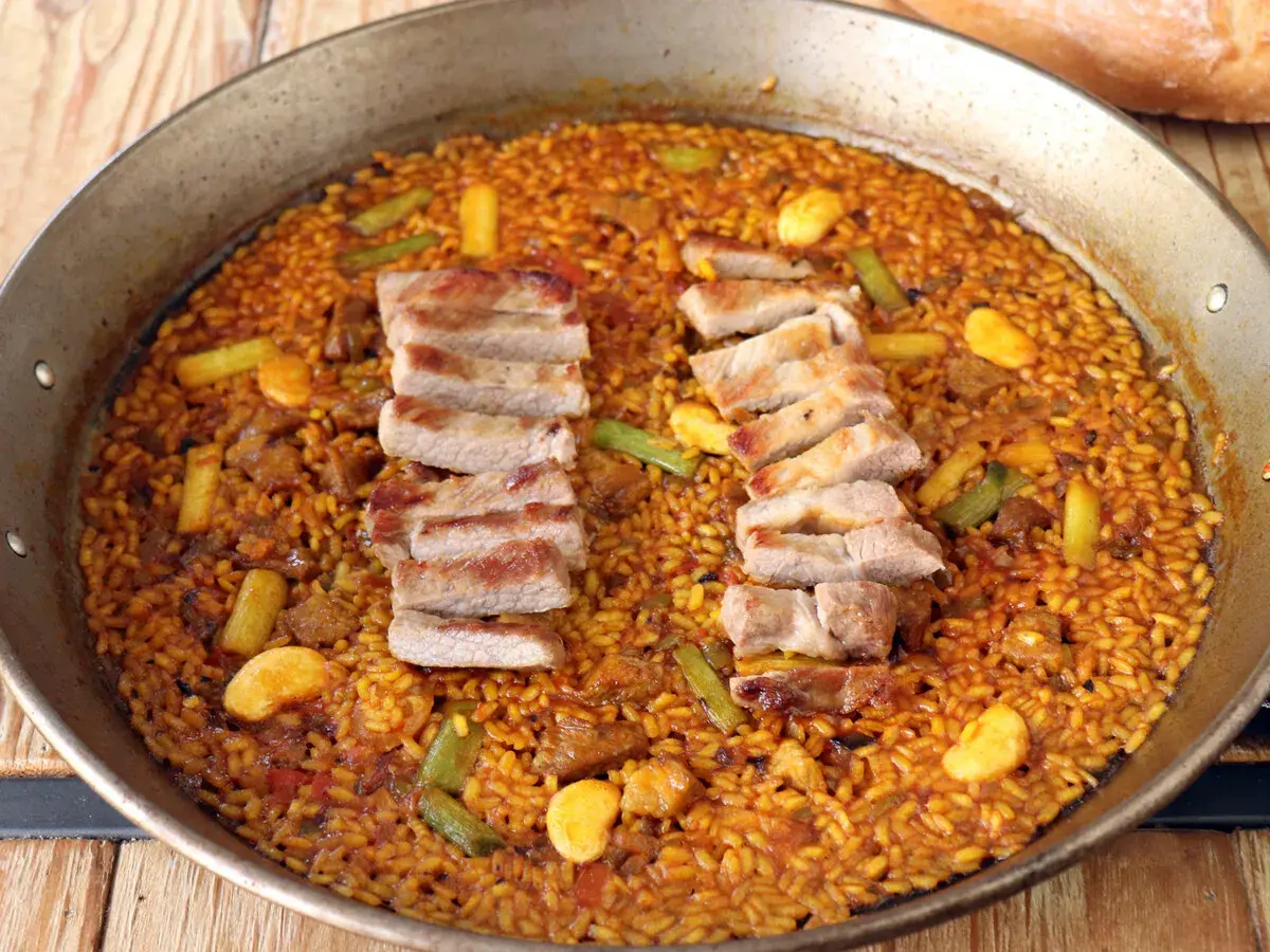 Arroz con secreto de cerdo, jugoso y dorado, con trozos de carne y verduras en una paellera.