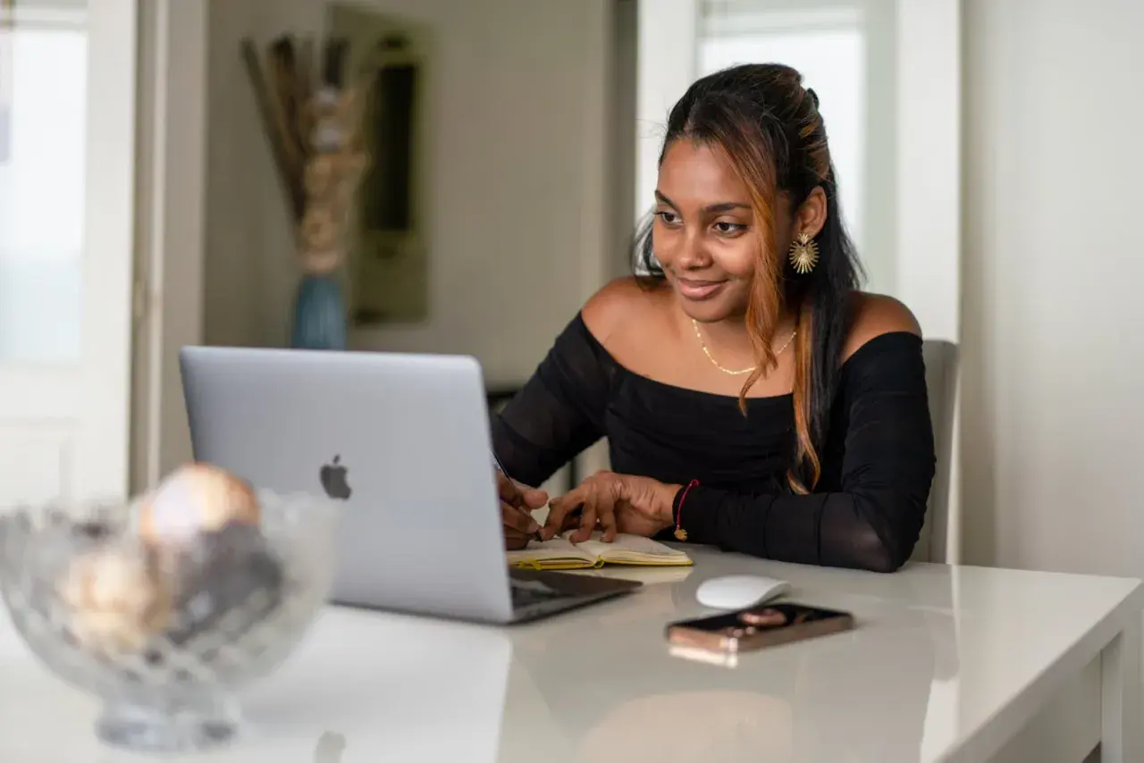 Giovane donna sorride mentre studia o lavora al computer, forse per insegnare inglese online.