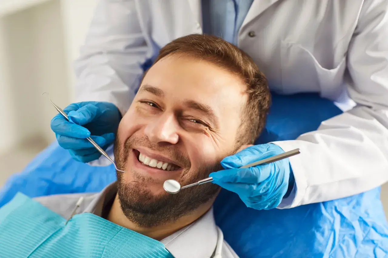 Uśmiechnięty mężczyzna u dentysty. Badanie stomatologiczne, które może pomóc rozwiać wątpliwości dotyczące implantów zębowych a nowotworów.