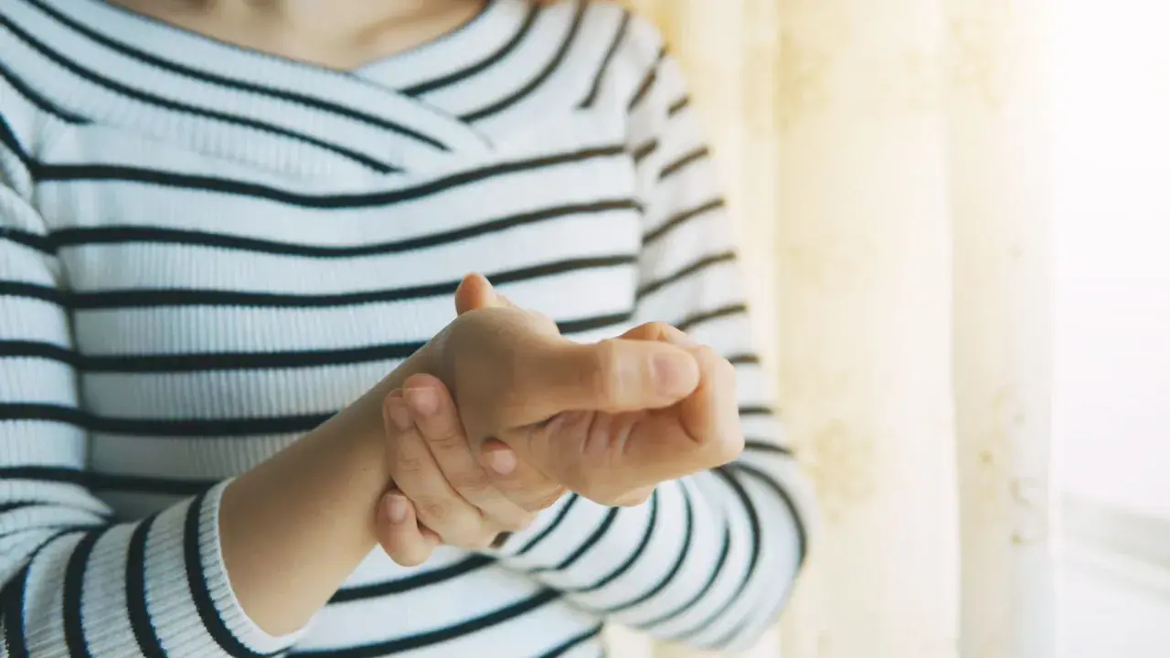 Frau hält ihren Daumen, der schmerzt, als ob sie einen Schnappfinger Daumen hätte.